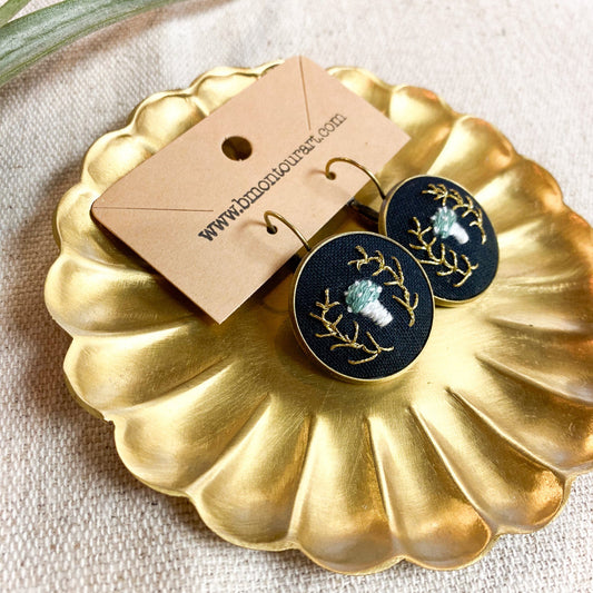 Pair of earrings on a gold dish with a visible brand tag
