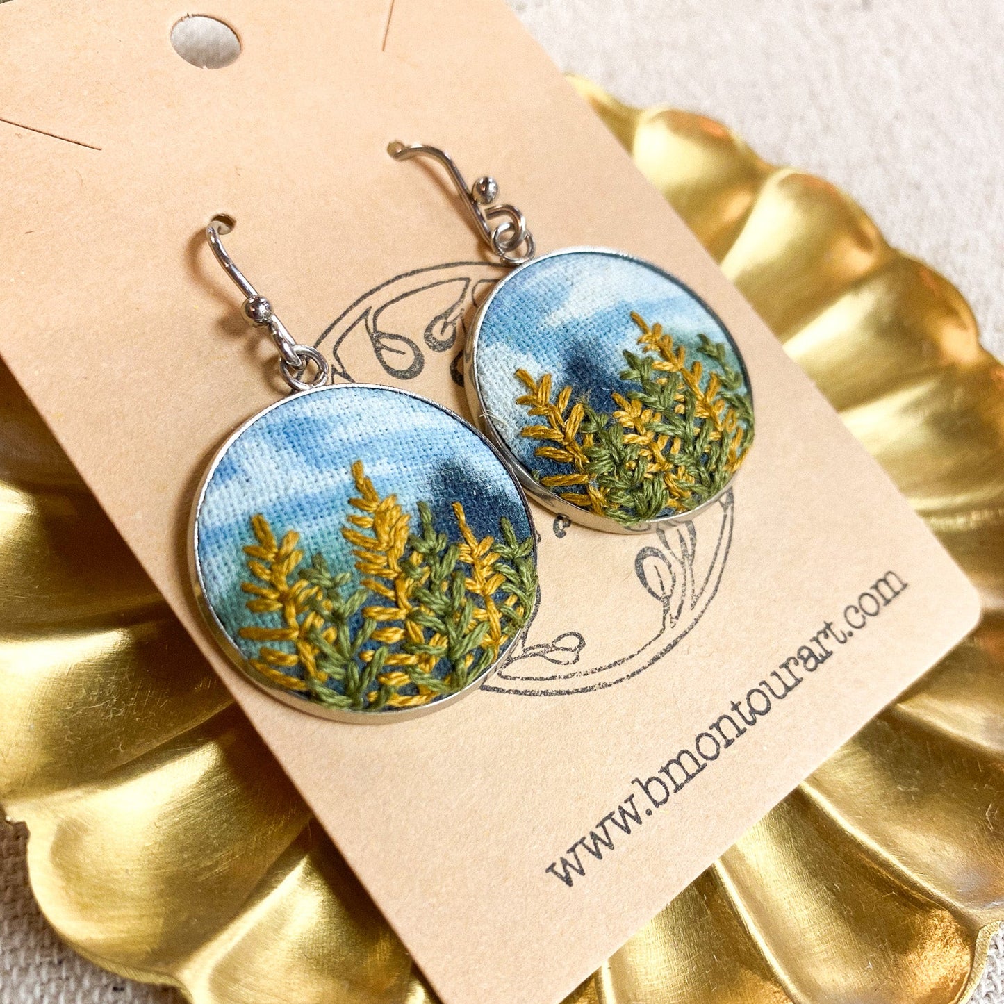 Pair of earrings with nature-themed design on a gold stand with a beige card.