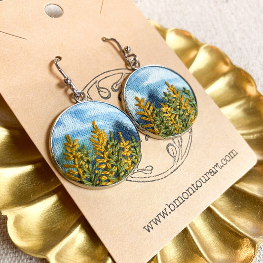 Pair of earrings with nature-themed design on a gold stand with a beige card.