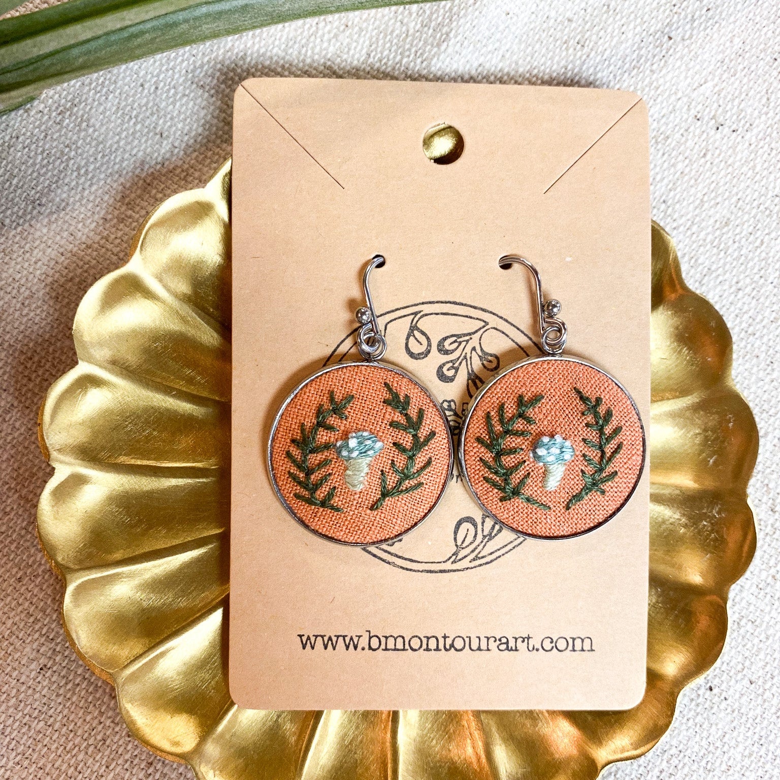 Earrings on a gold display stand with a beige card showing 'www.bmonourart.com'.