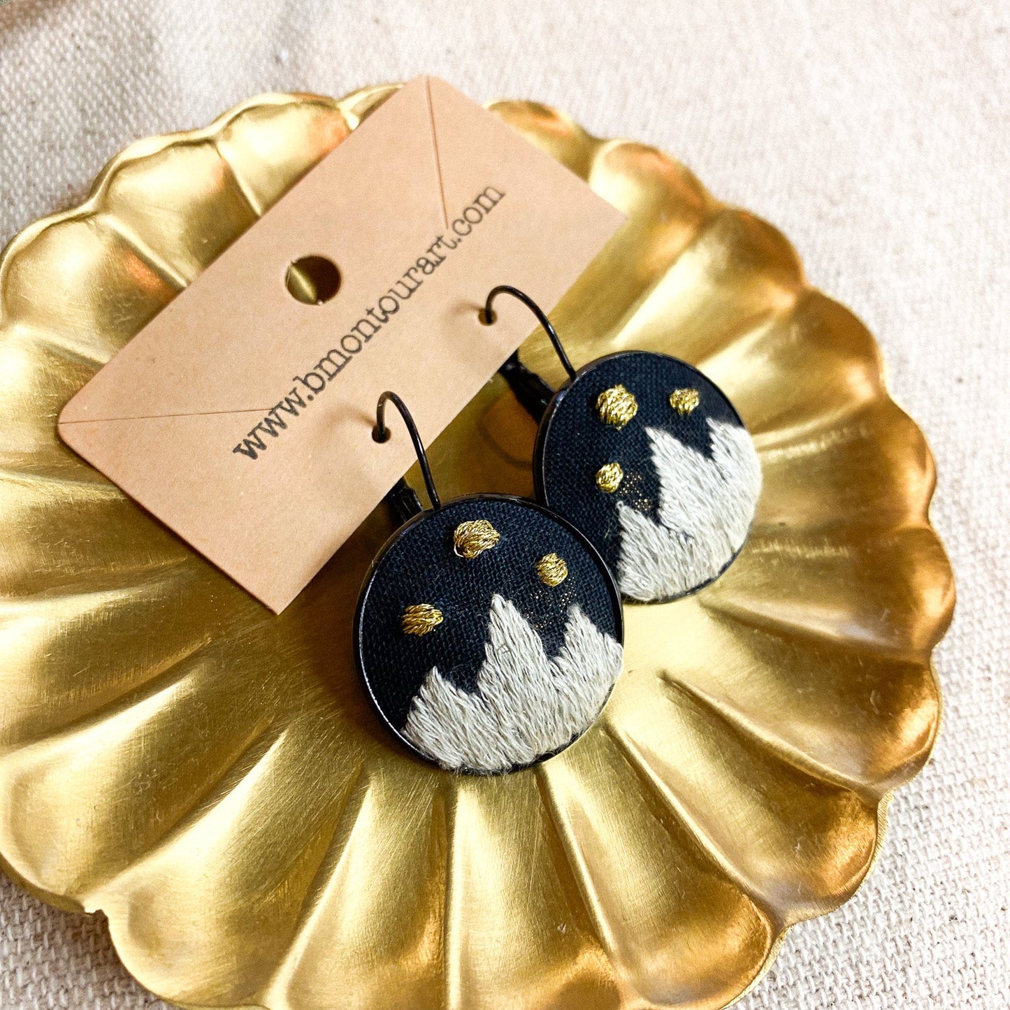 Pair of earrings on a gold display stand with a branded card.
