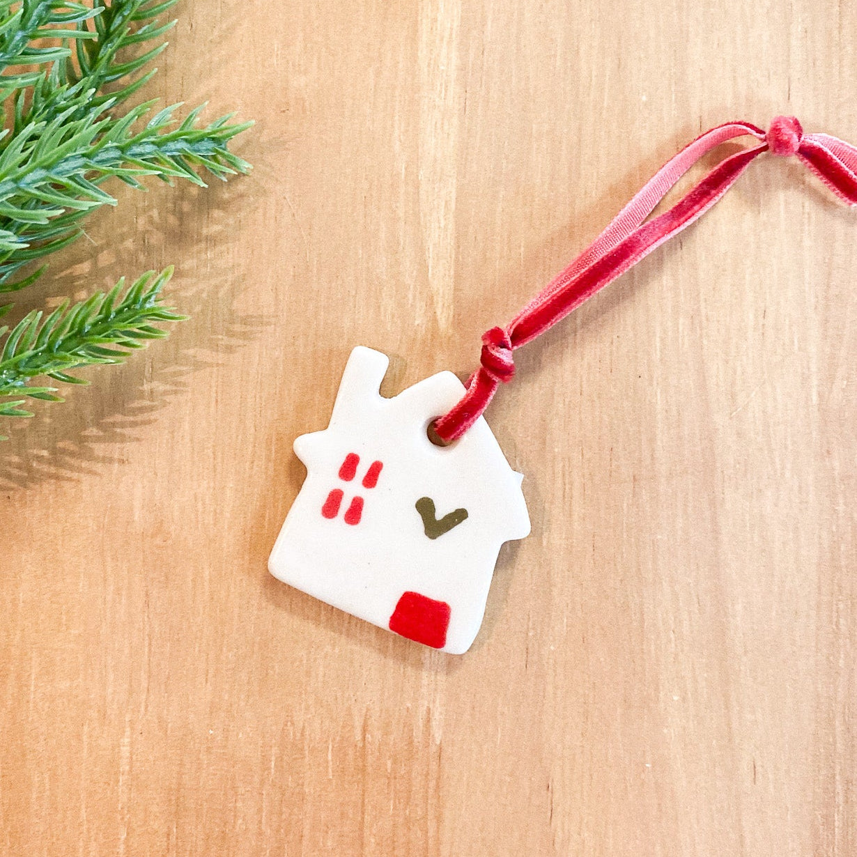 Decorative house ornament with a red ribbon on a wooden surface with greenery.