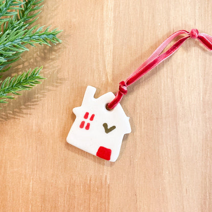 Decorative house ornament with a red ribbon on a wooden surface with greenery.