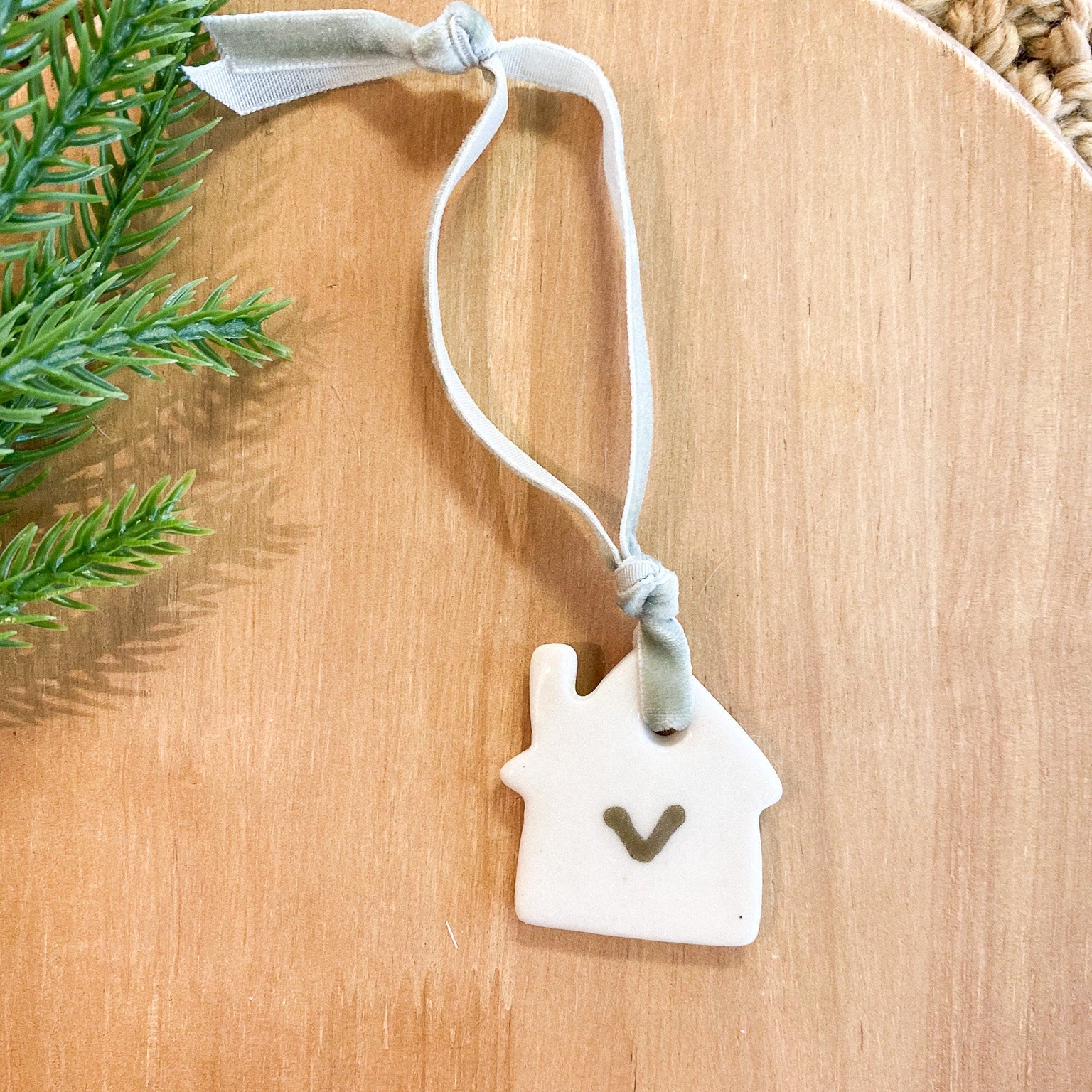 White house-shaped ornament with a heart on a wooden surface with greenery