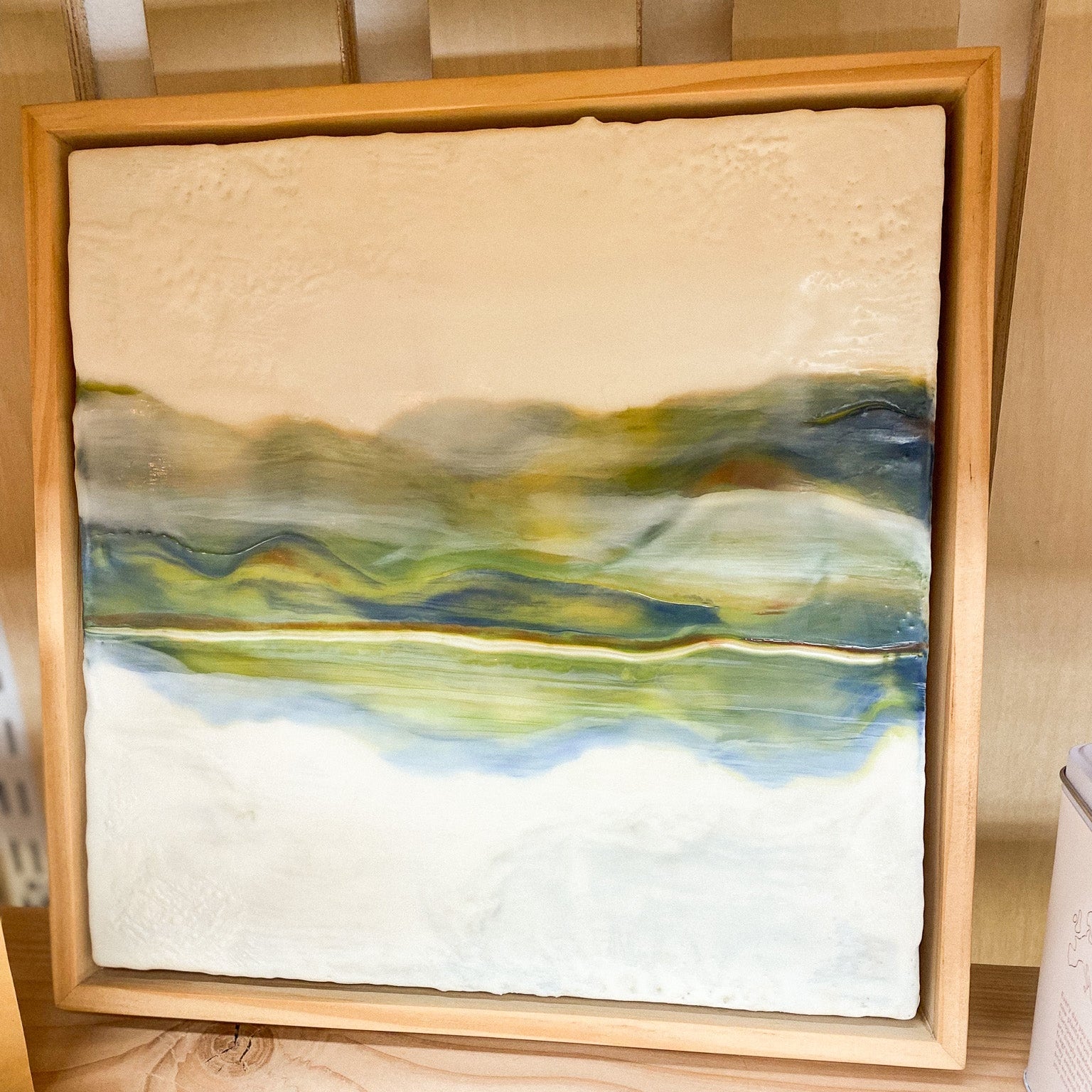 Framed abstract painting with earthy tones on a wooden surface