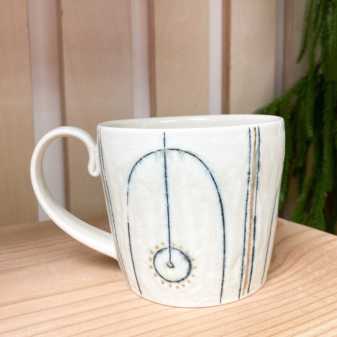 White ceramic mug with decorative design on a wooden surface with a plant in the background