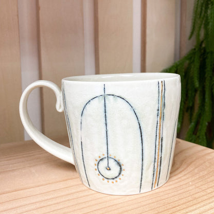 White ceramic mug with decorative design on a wooden surface with a plant in the background