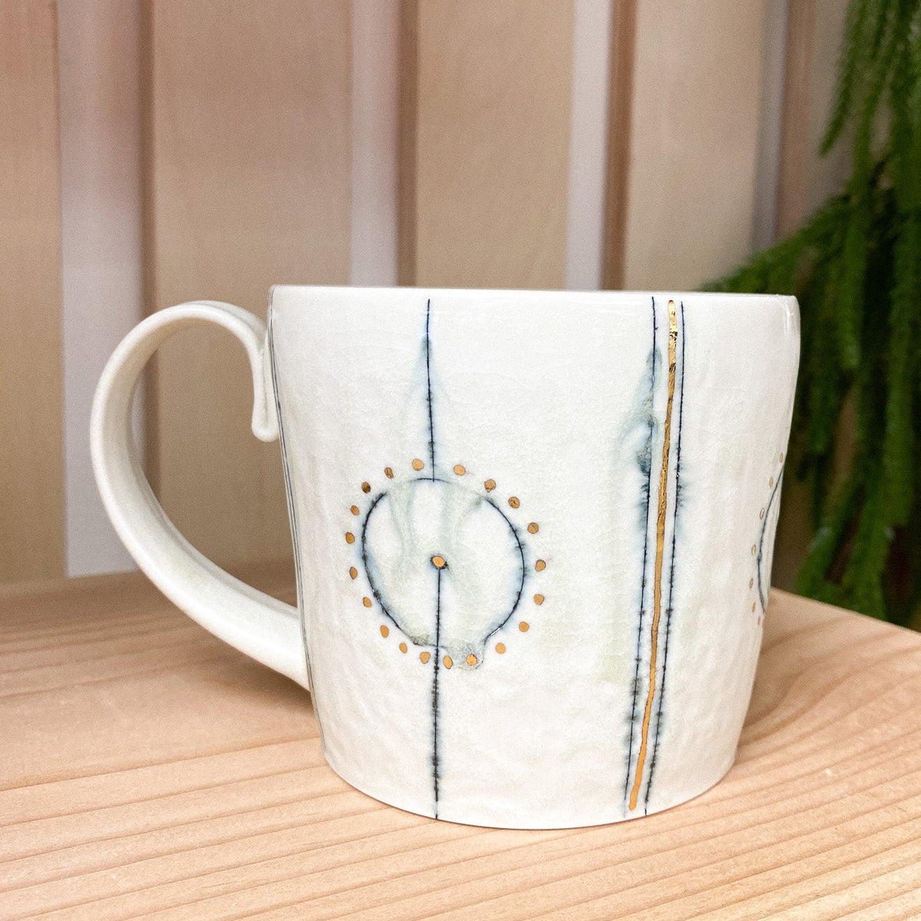 White ceramic mug with decorative patterns on a wooden surface with a plant in the background