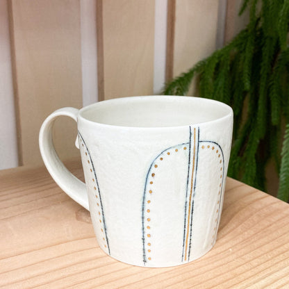 White mug with decorative patterns on a wooden surface with a blurred green plant in the background