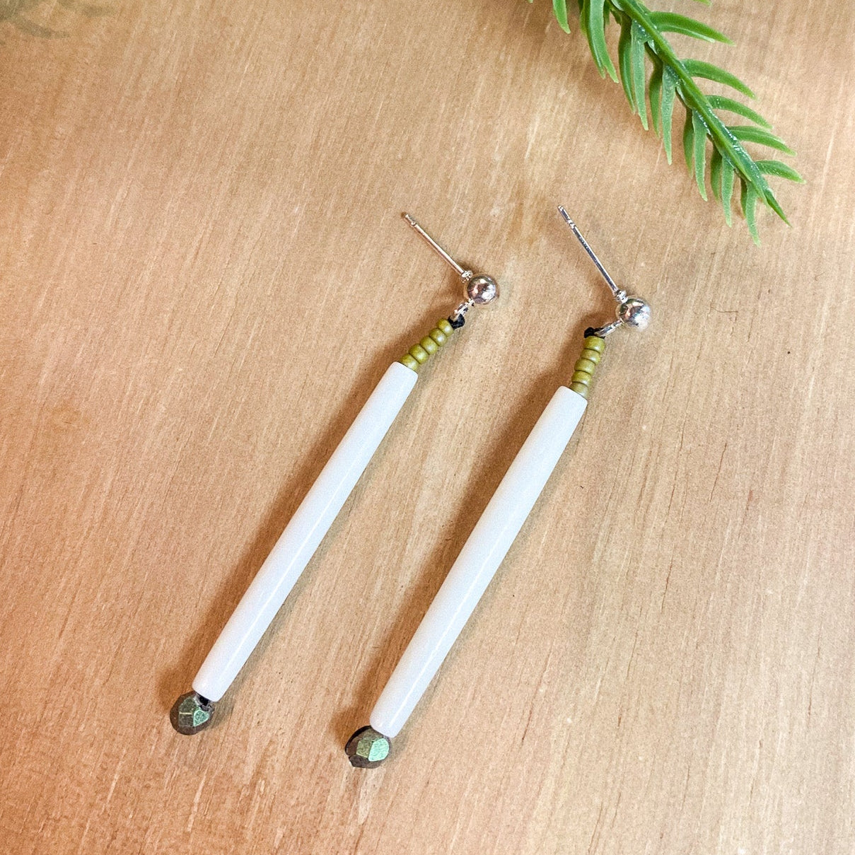 Pair of dentillium earrings on a wooden surface with green leaves in the background