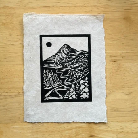 Black and white mountain landscape design on a textured white card against a wooden background