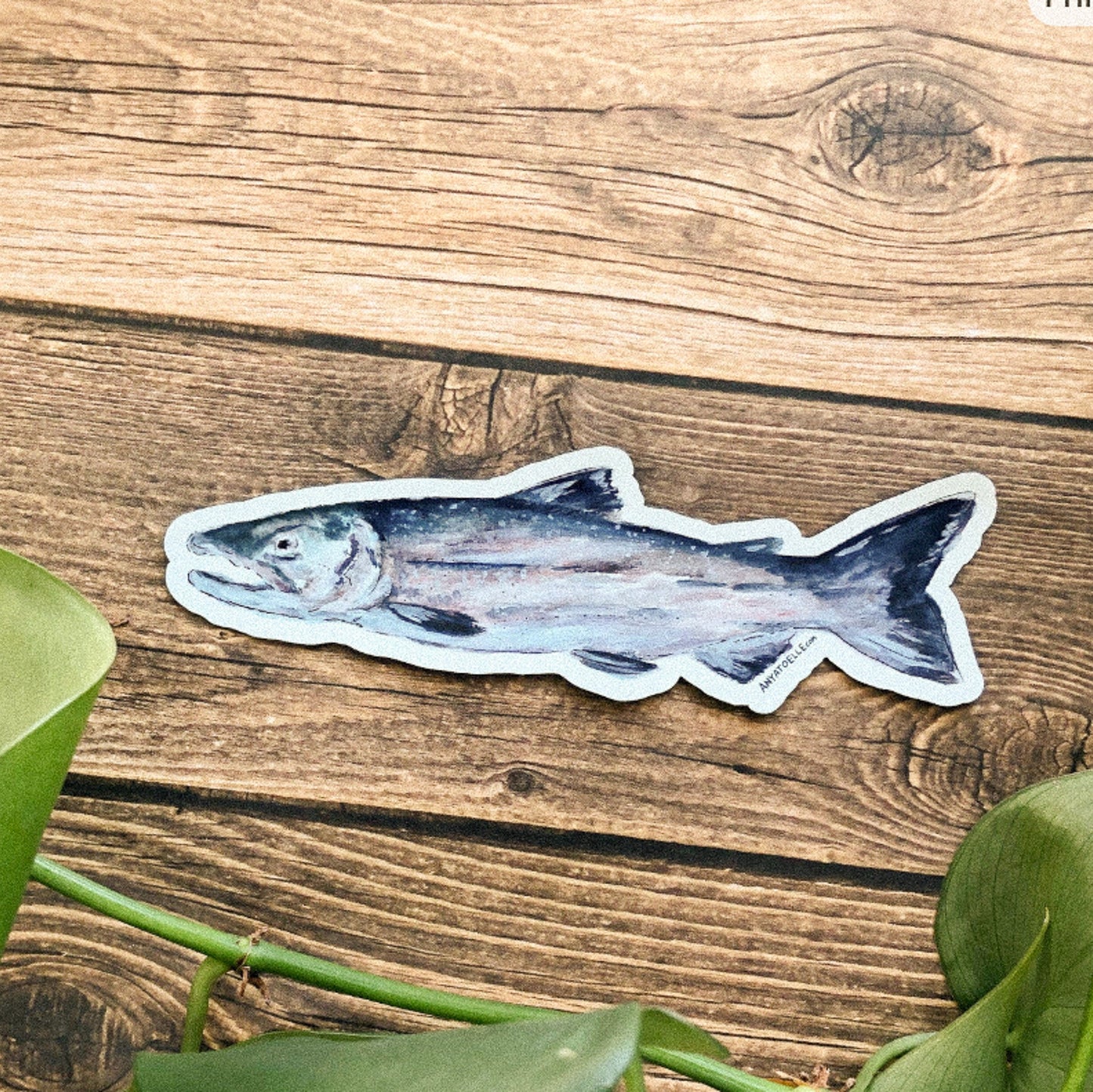 Fish magnet on a wooden surface with green leaves