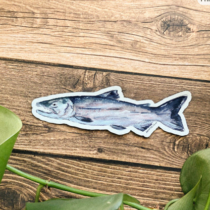 Fish magnet on a wooden surface with green leaves