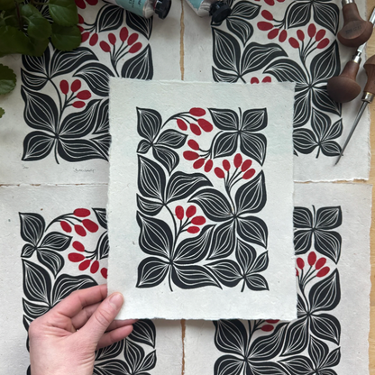 Handmade fabric with black and red floral patterns, surrounded by paint tubes and tools on a wooden surface.