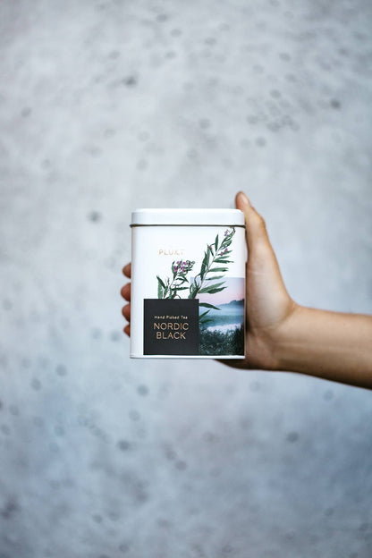 Hand holding a tea canister with a scenic label against a gray background